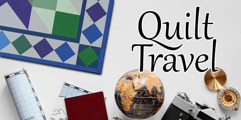 Banner image featuring the words 'Quilt Travel' in elegant script, with a colorful geometric quilt pattern in the background, a globe, compass, travel maps, a passport, and a camera, representing themes of travel and quilting.